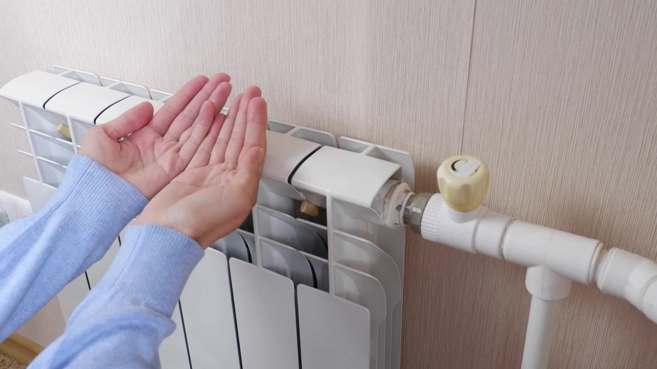詳情圖-一名女性在家里的房間里用電池和加熱器取暖。手指，手掌保持暖氣片的溫度，靠近。室溫較低。冬季取暖期、季節(jié)。