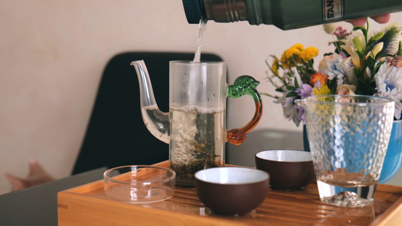 一名男子將熱水瓶里的開水倒入盛有白茶的玻璃器皿中沖泡。中國茶道