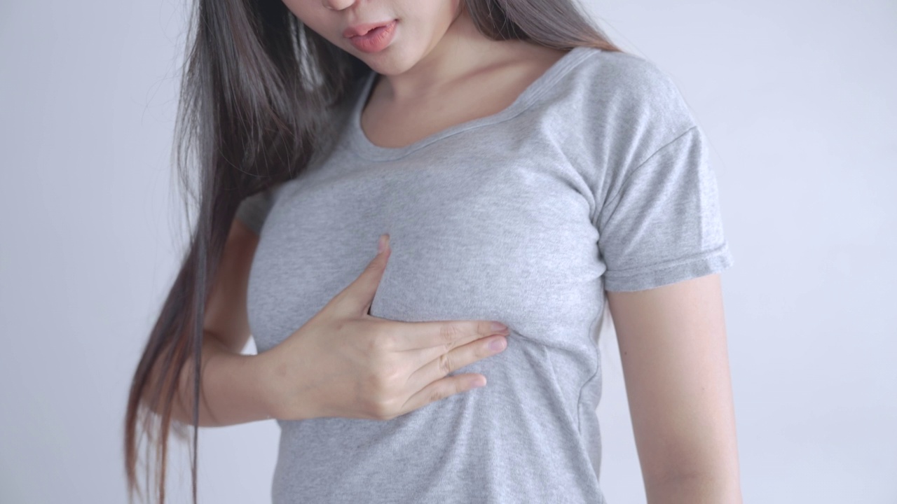 一名穿着灰色t恤的亚洲女性正在自我检查是否患有乳腺癌。
