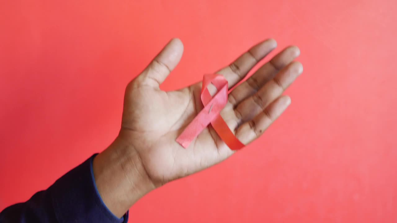红色背景下，手拿红色HIV丝带