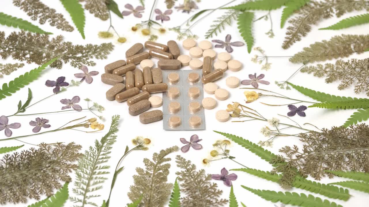 药用胶囊与干燥的药材在白色背景旋转慢动作。草药，顺势疗法，替代医学，有机药学概念