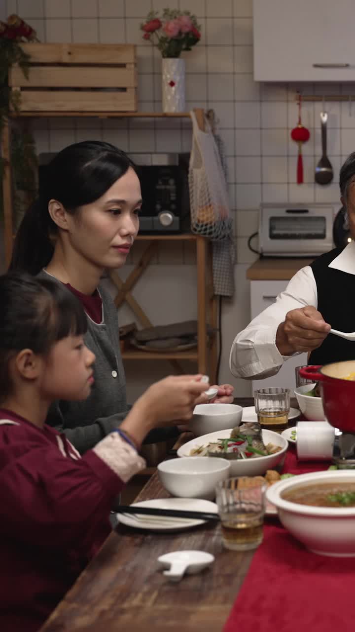 竖屏:亚洲大家庭晚上聚在一起吃年夜饭时，用勺子吹着美味的热汤，品尝着