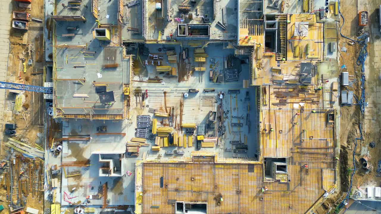 空中飞行在一个新的建筑开发现场与高塔起重机建设房地产。雇用重型机械和建筑工人。从上往下看戴安全帽的承包商。
