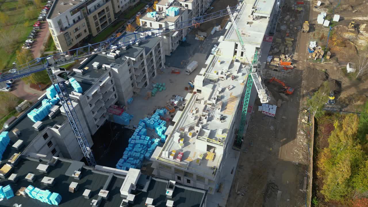 空中飞行在一个新的建筑开发现场与高塔起重机建设房地产。雇用重型机械和建筑工人。从上往下看戴安全帽的承包商。