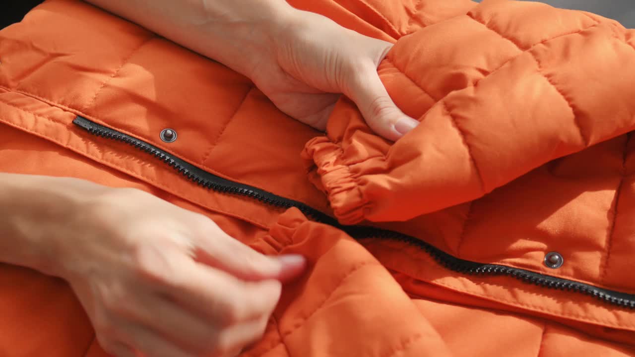 女性手摸摸材质橙色防水面料的冬季夹克、羽绒服。纺织、制衣、秋亮夹克。时尚,风格。衣服的背景