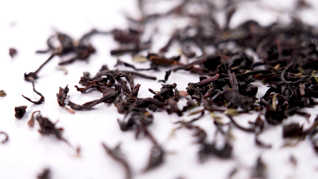 百里香红茶干叶子慢动作落在白色碟子上。草药饮料。旋转