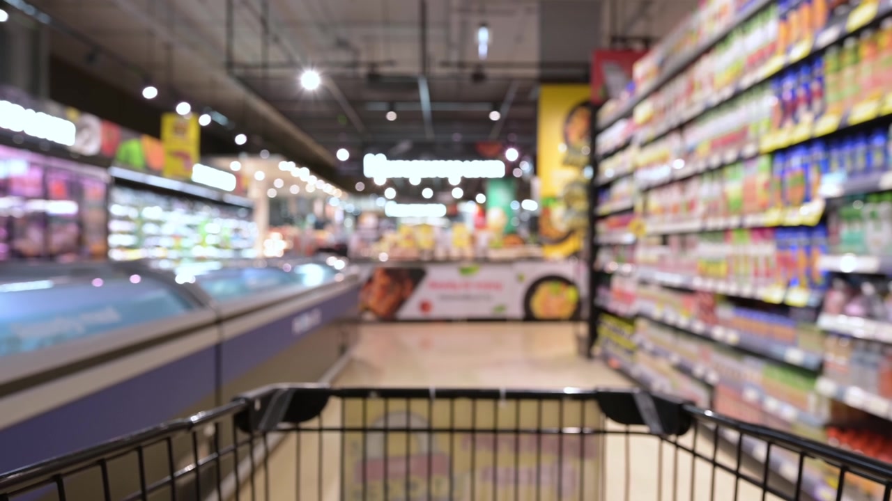 详情图-模糊的购物车通过食品货架内部散焦背景在超市。一个人在超市里推着购物车的慢动作镜头。