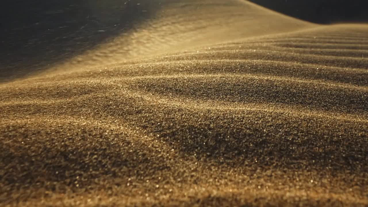 沙漠中的沙塵暴。微距拍攝的沙粒被風吹走。在落日的余暉中，攝像機沿著沙漠中的沙丘表面移動。沙子在風中飄動。慢鏡頭