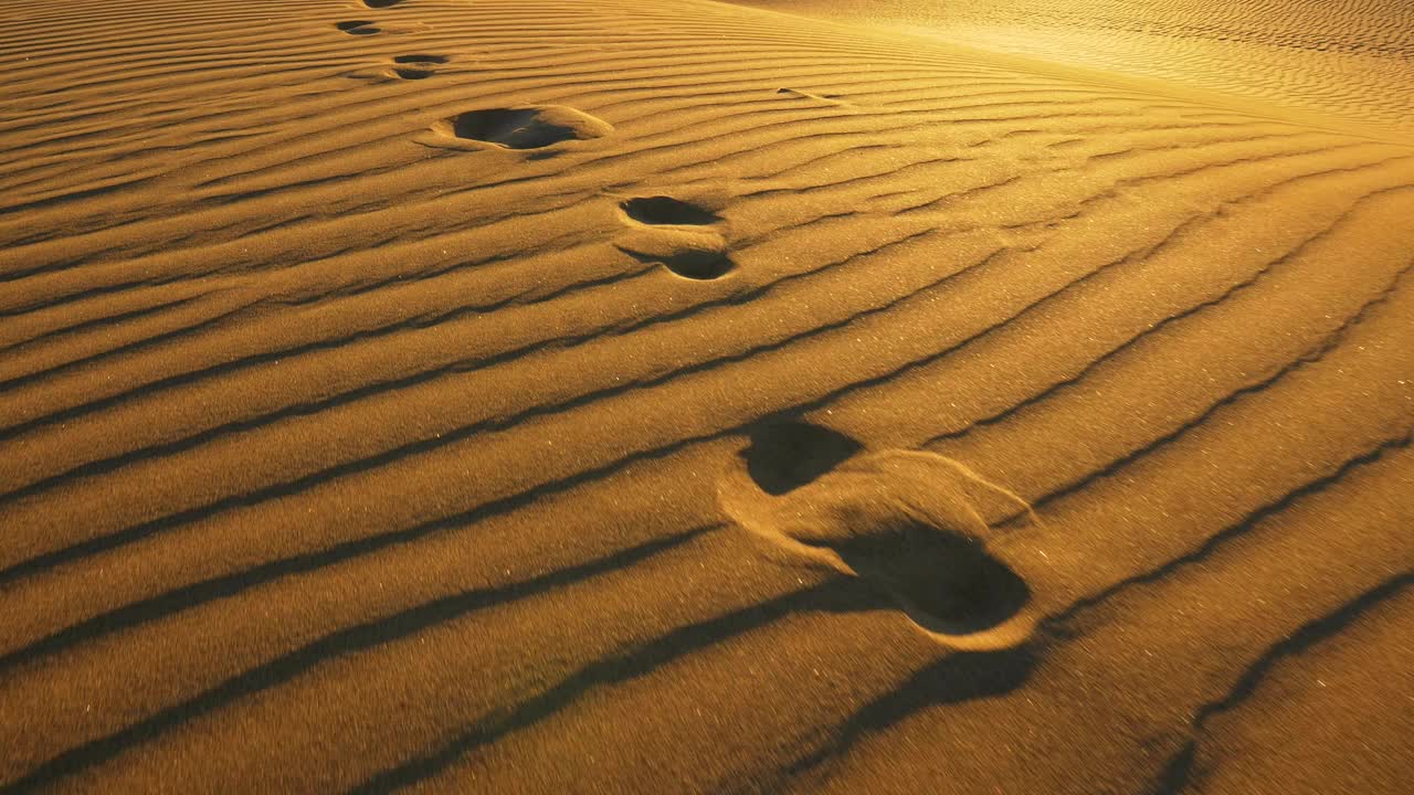 摄像机追踪大沙丘上的脚印。温暖的夕阳下，沙漠里沙滩上的脚印。UHD 4 k