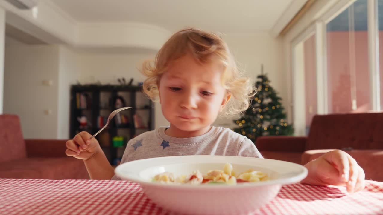 孩子在厨房的桌子上吃通心粉加番茄酱。妈妈给孩子加了番茄酱。不良饮食习惯