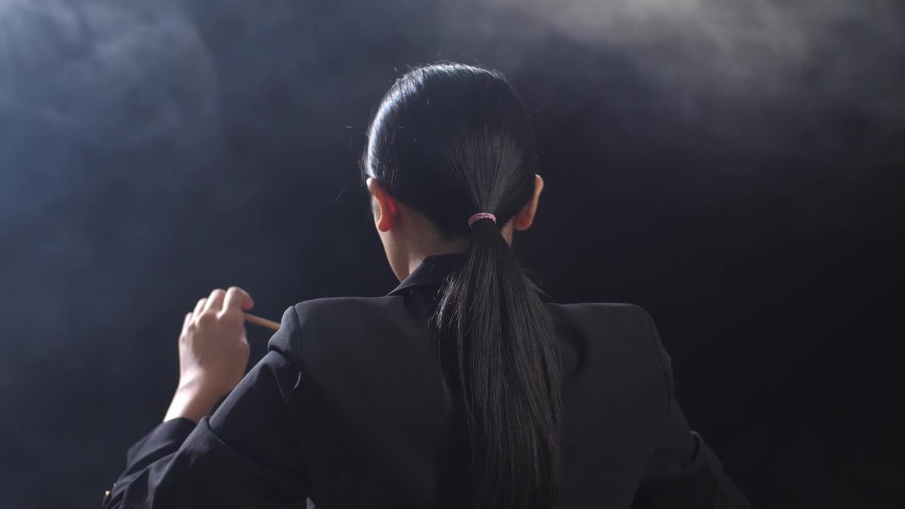 亚洲指挥家女子拿着指挥棒，在黑色工作室与雾快速展示手势的特写