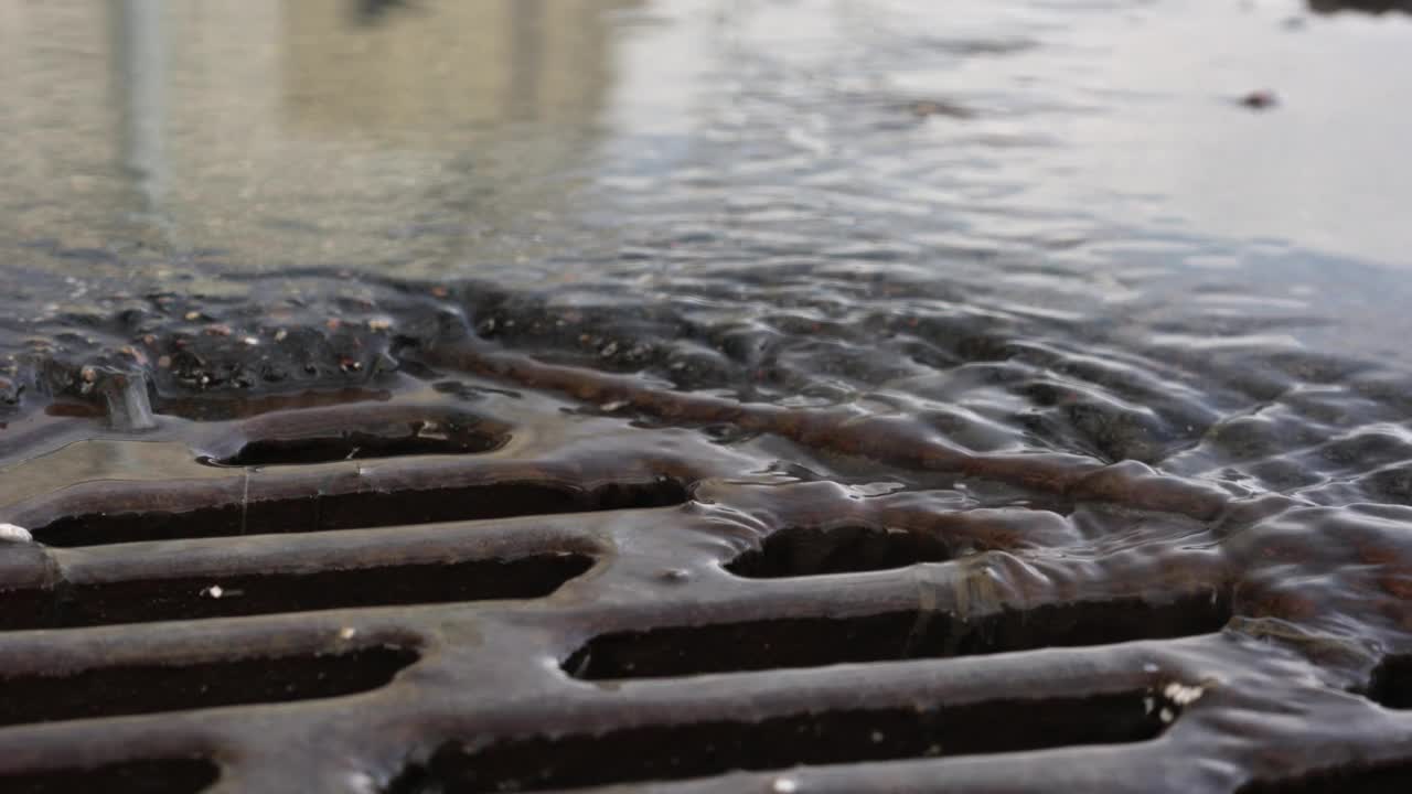 雨水在生锈的金属路网的人孔中流动。