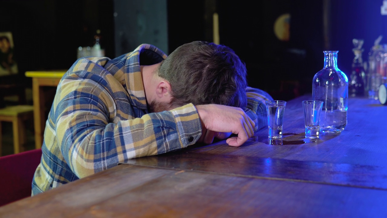 一个喝得酩酊大醉的年轻人头靠在酒吧的桌子上