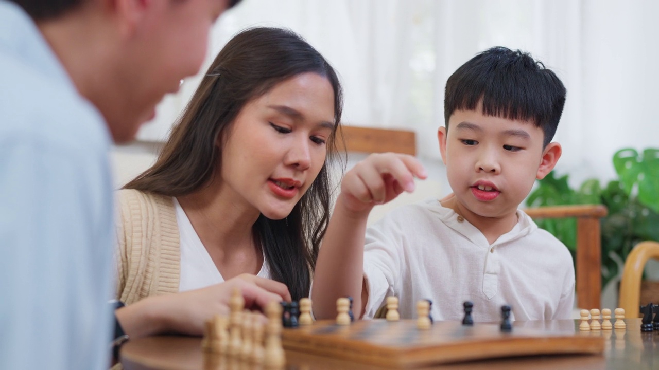 快乐的亚洲家庭，爸爸妈妈和儿子一起在家里的客厅下棋。孩子们学下棋。假期的爱好。规划和战略概念。父母关系。