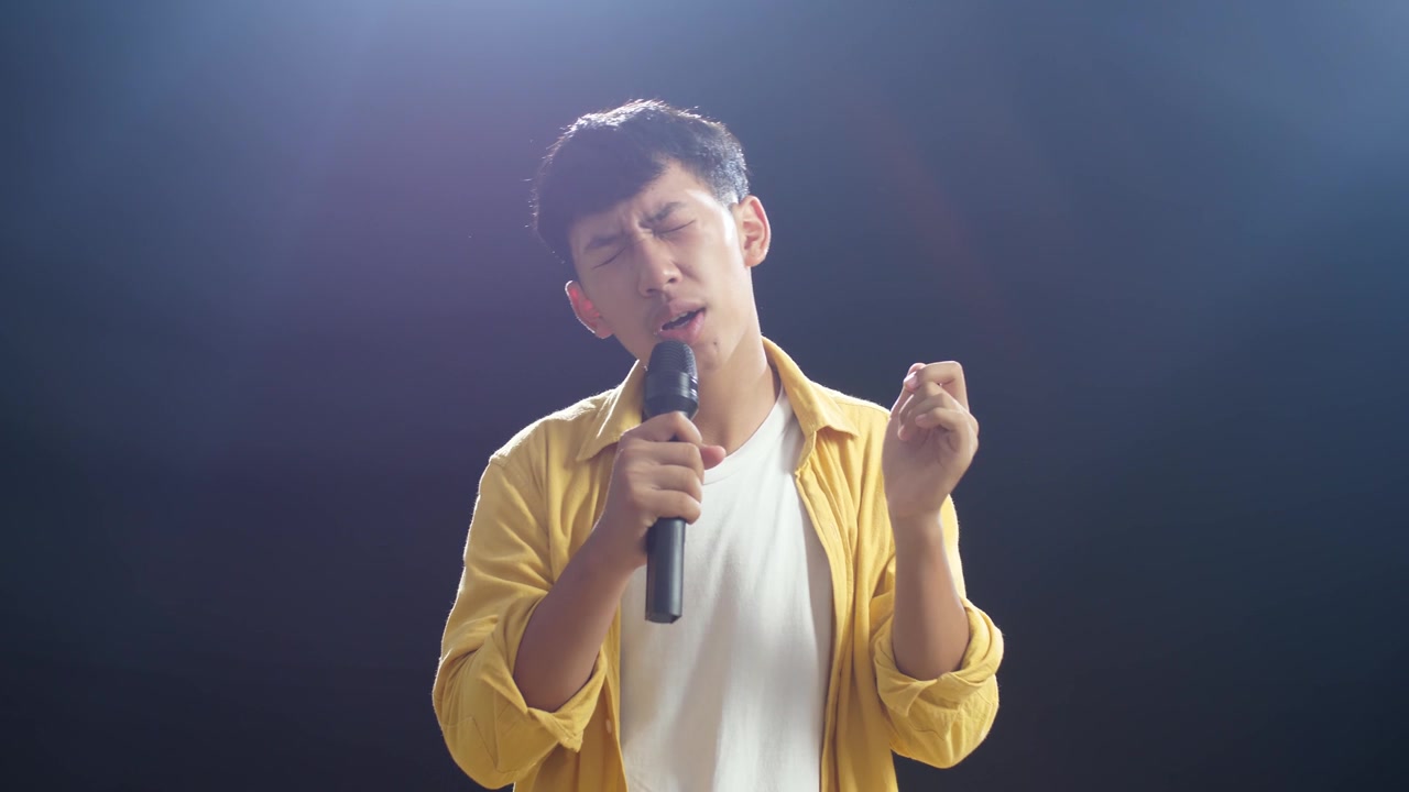 详情图-年轻的亚洲男孩拿着麦克风，在黑色背景上唱歌
