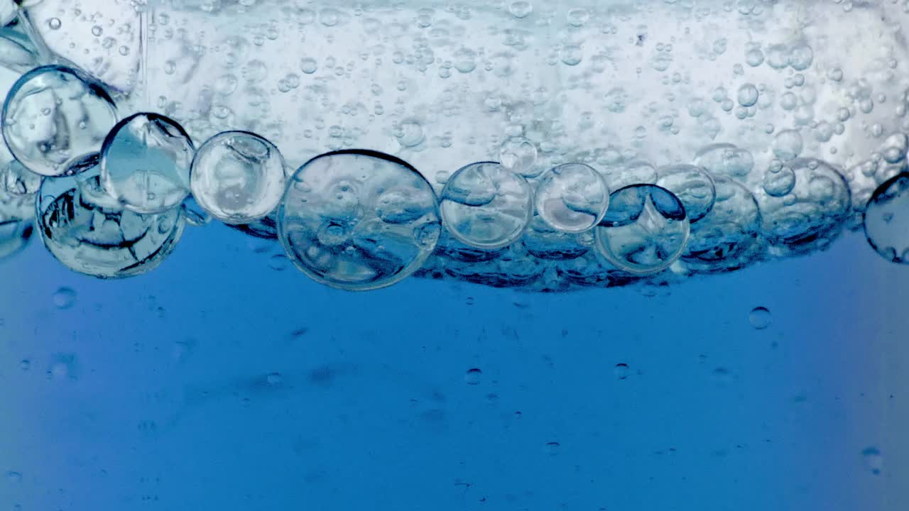 移动的红色石油的慢动作，气泡在水中上升在轻白色背景。带有气泡的透明化妆凝胶液。微距镜头。