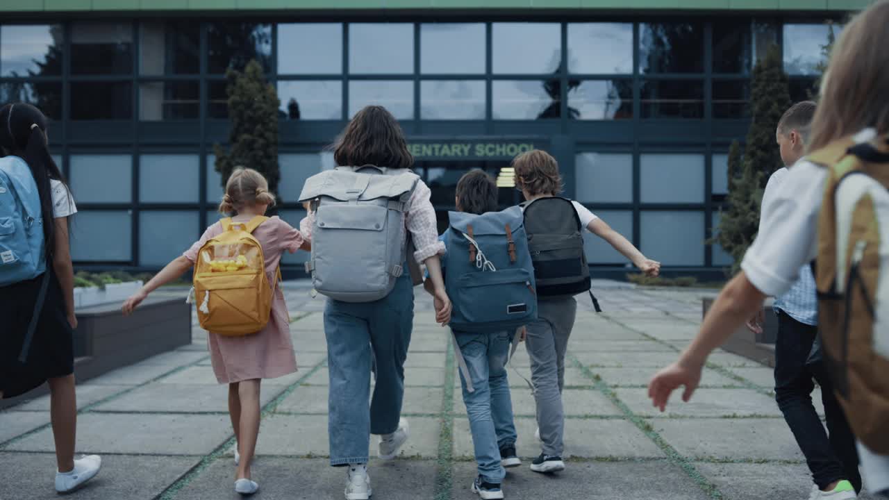 不同的孩子背着书包上学。欢迎青少年学生的老师