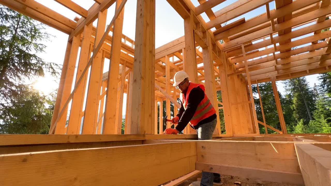 木匠在森林附近建造木制框架的两层楼房时，正在敲打钉子。