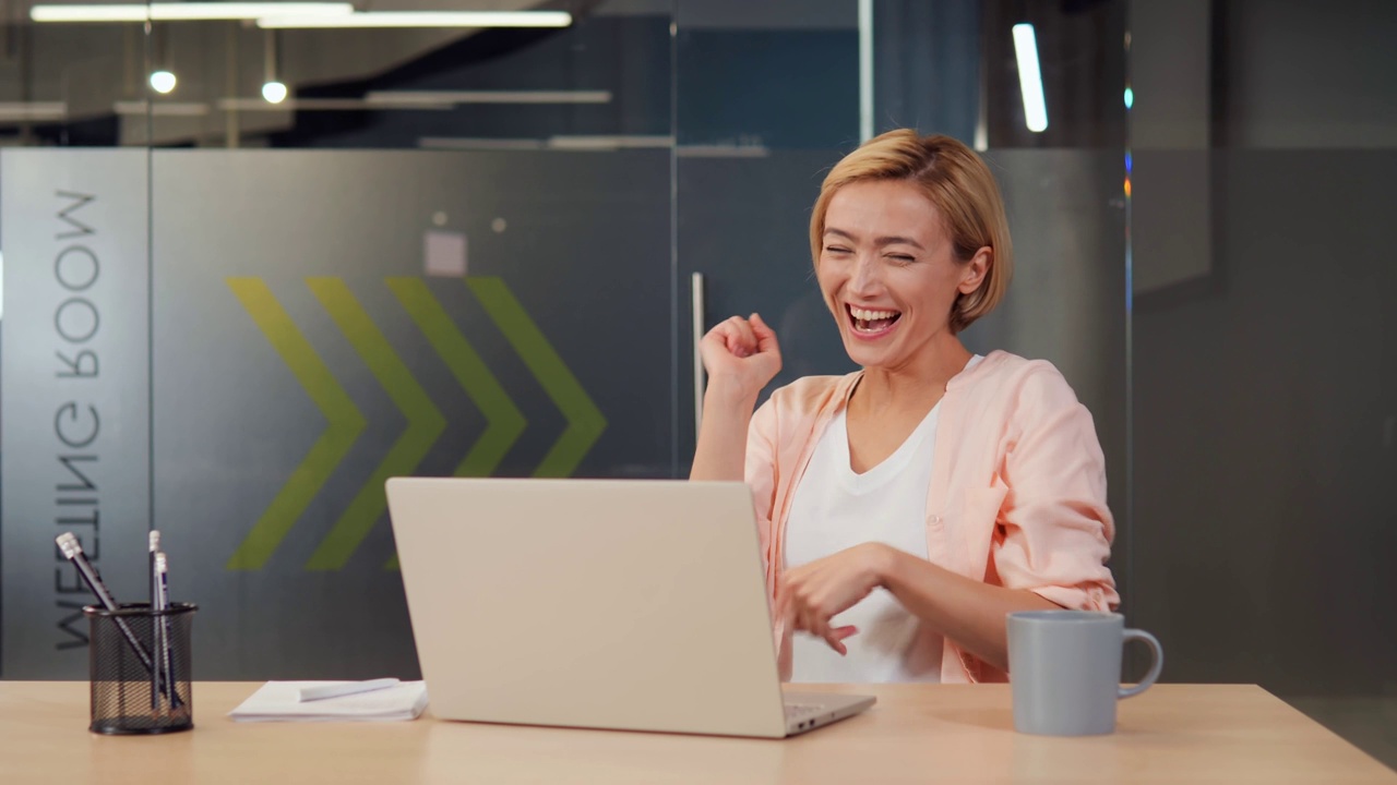 詳情圖-美麗，開朗，精力充沛的女人在她的筆記本電腦上收到一個獲勝的通知。女孩因成功和勝利而欣喜若狂。她燦爛的笑容和正能量可以照亮整個房間。