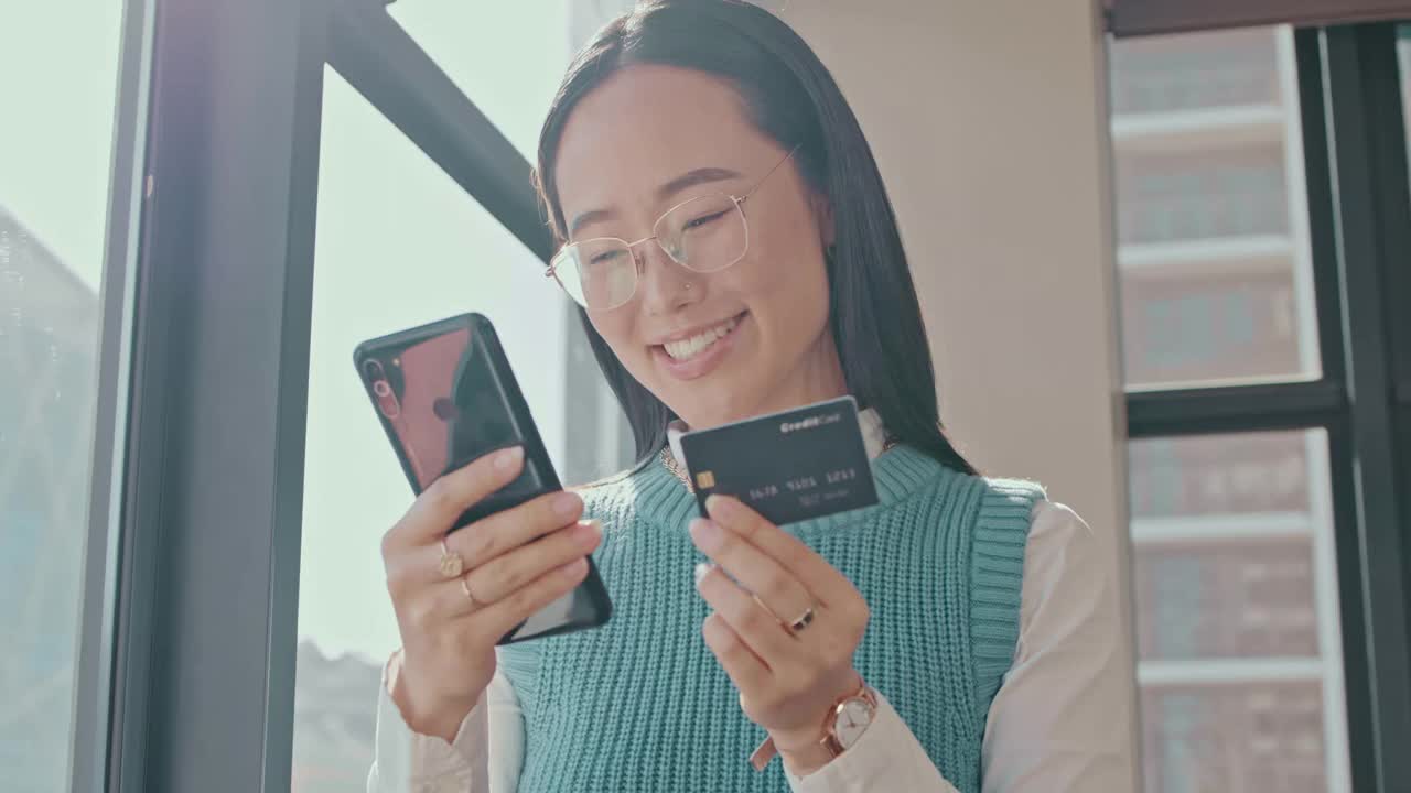 快乐的亚洲女人，电话和信用卡网上购物，电子商务或电子交易。兴奋的女性微笑着在室内通过手机应用程序或网上银行进行无线购物