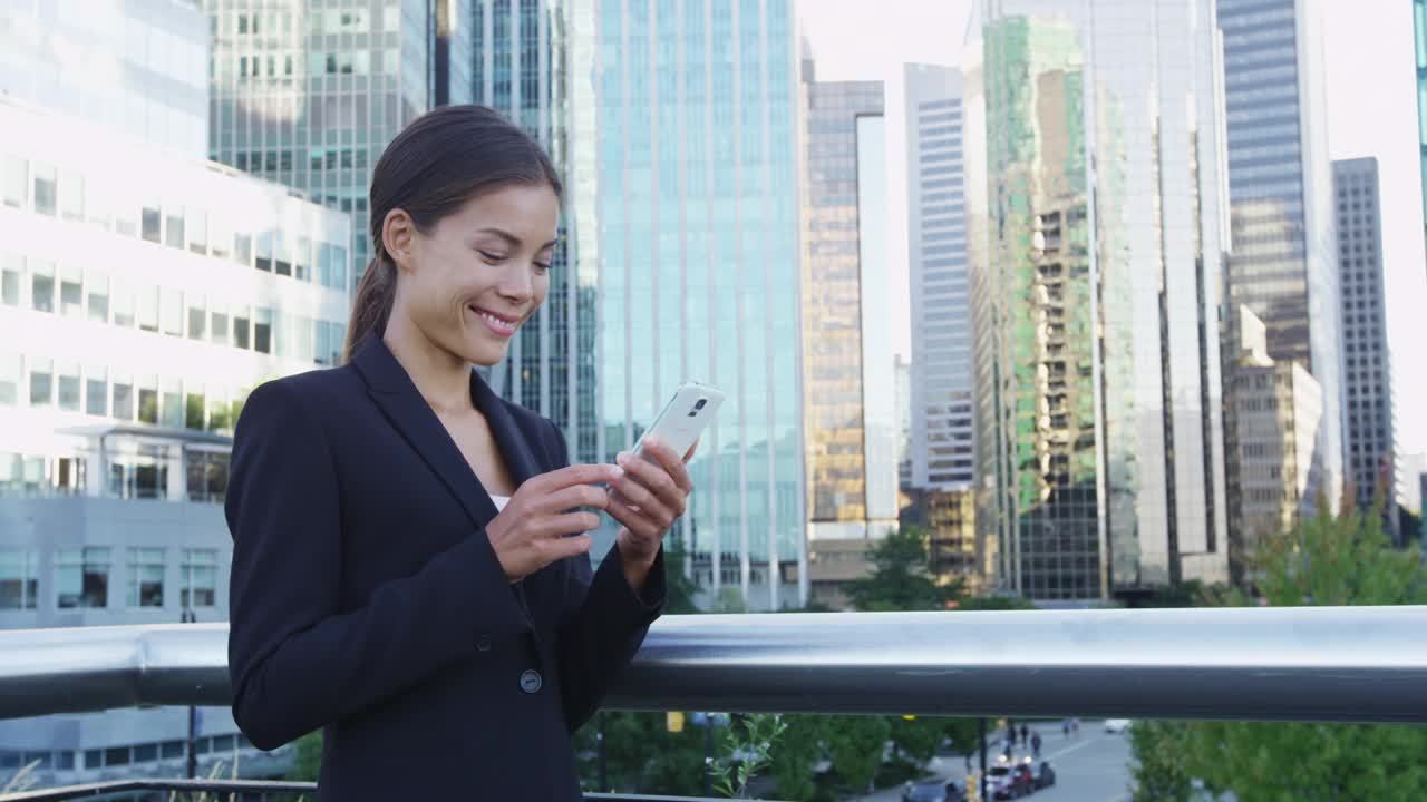 一名女子在温哥华商业区用手机上的应用程序发短信。穿着西装外套使用智能手机的年轻女商人。20多岁的城市女性专业人士。公元前,加拿大。