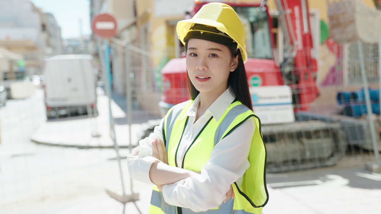 年轻的中国女建筑师微笑着自信地站在街上，双臂交叉