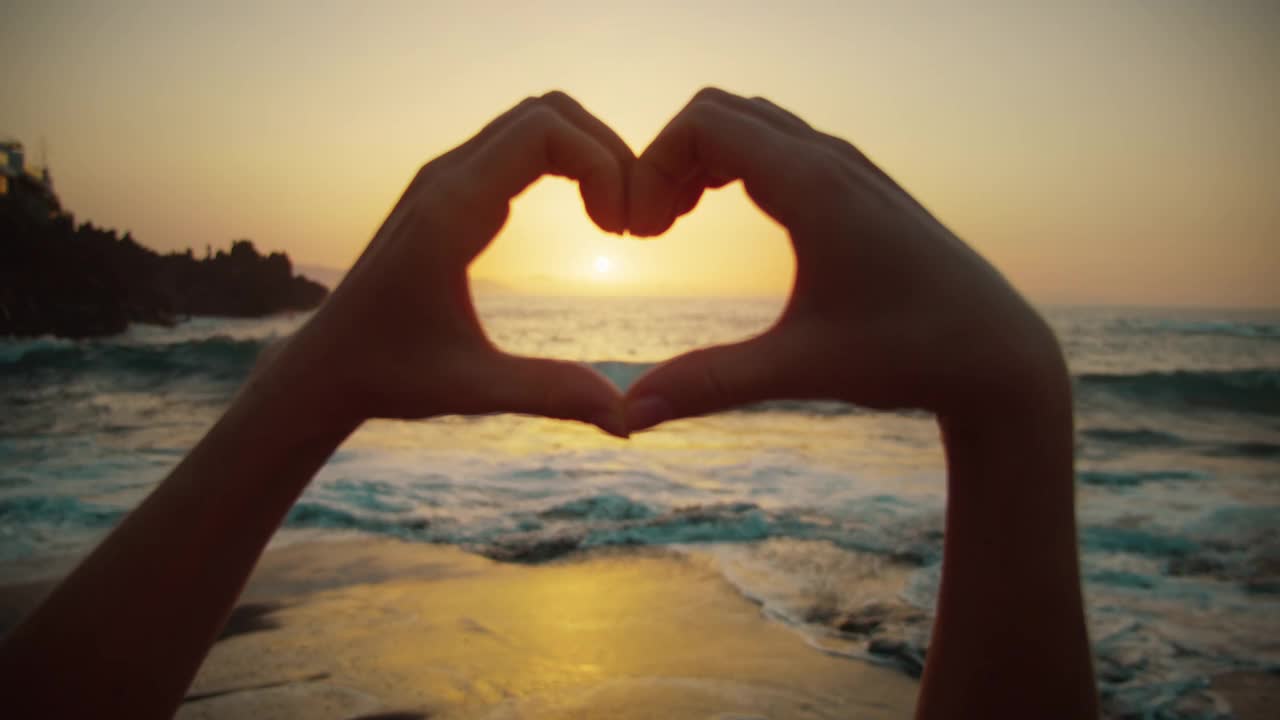 女性的手在金色的夕阳映衬下露出心形的标志。暑假旅行者做梦。指缝间的阳光。