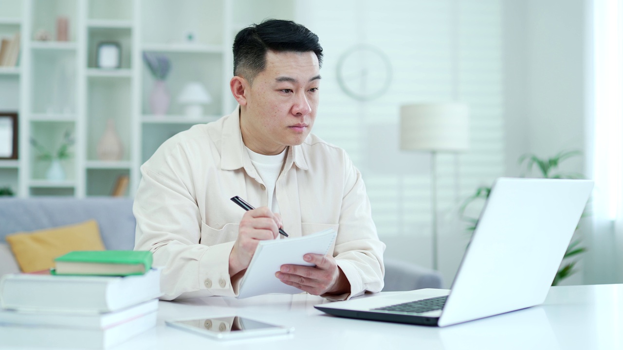集中亚洲人观看视频电话课程或培训，而坐在家里的办公室使用笔记本电脑。