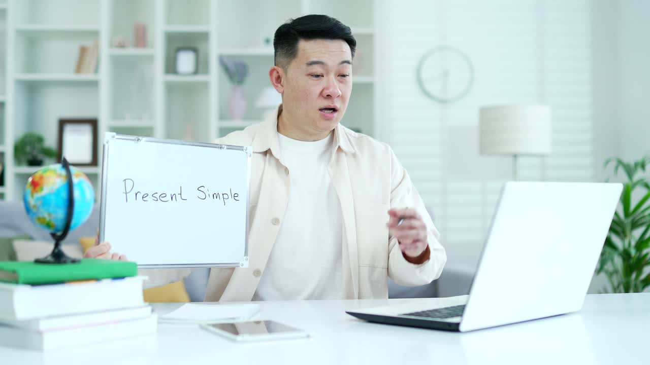 自信的亚洲私人教师，坐在家里办公室，用笔记本电脑通过视频电话给学生上英语课
