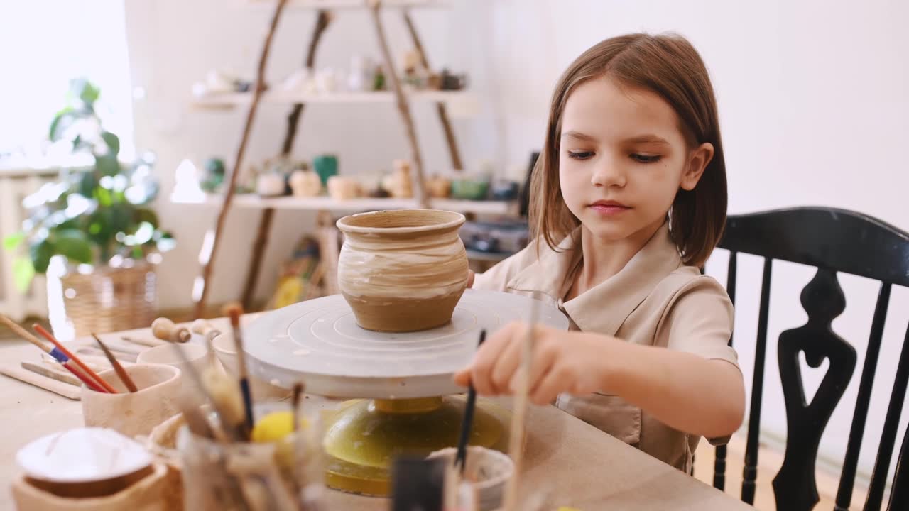 詳情圖-女孩正在用毛筆在鍋上畫畫。母親和她的小女兒正在做陶藝練習(xí)。