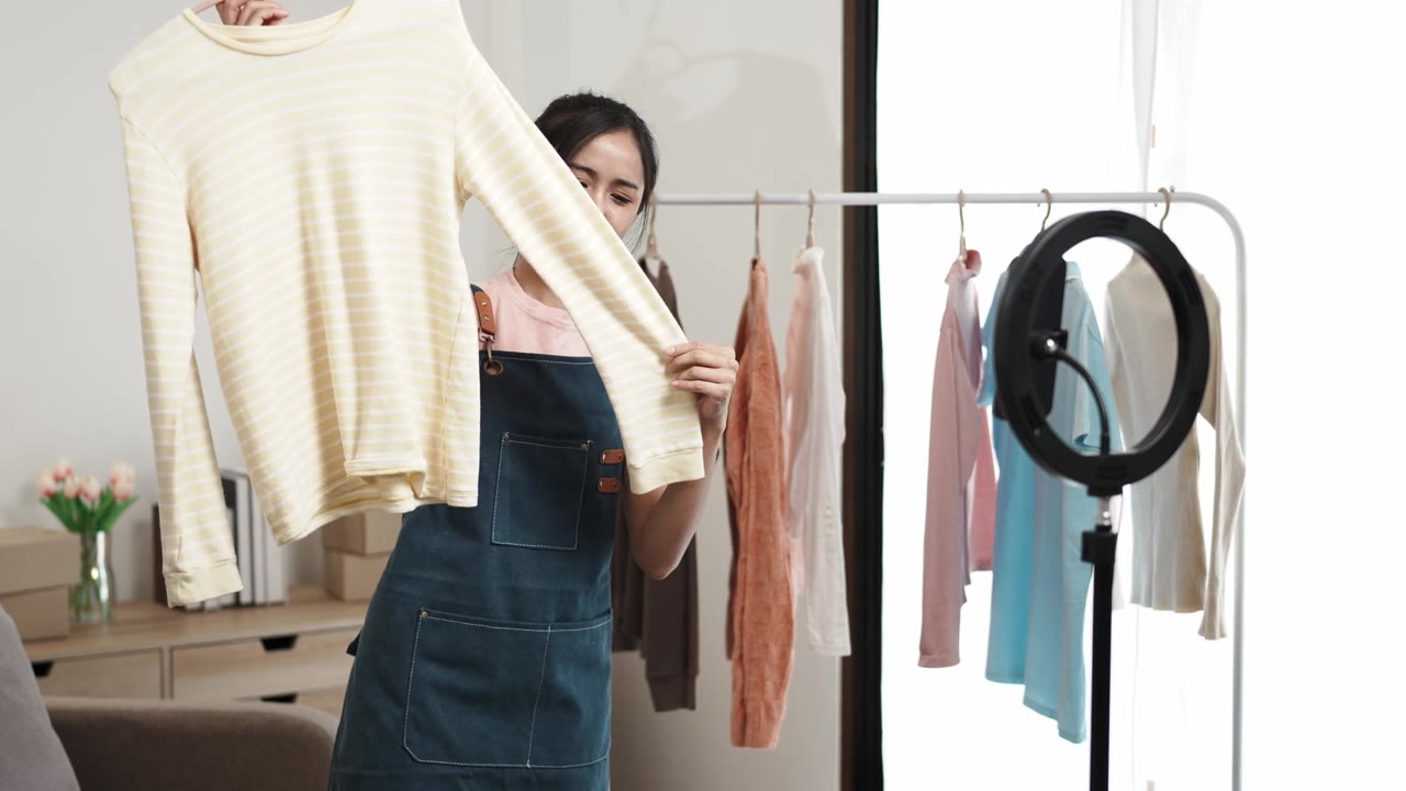 詳情圖-社交媒體市場(chǎng)概念。年輕的亞洲女賣家在移動(dòng)應(yīng)用程序的直播中展示二手衣服。