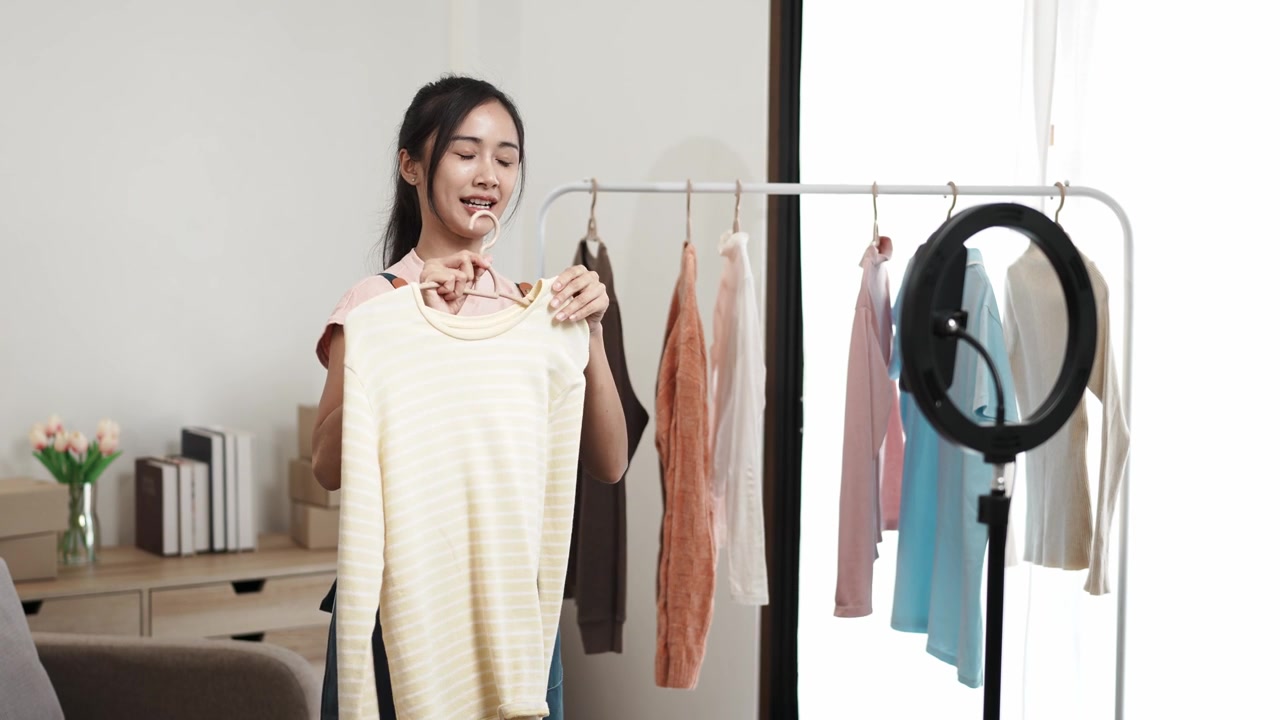 詳情圖-社交媒體市場(chǎng)概念。年輕的亞洲女賣家在移動(dòng)應(yīng)用程序的直播中展示二手衣服。