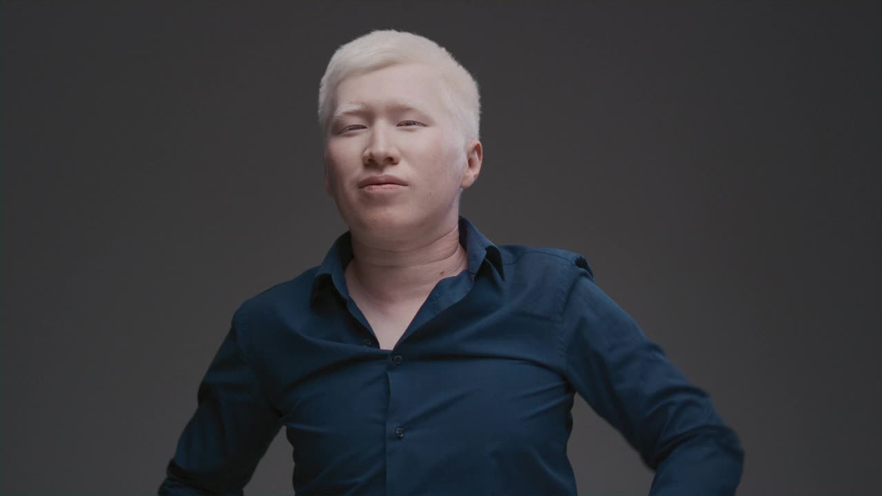 一个亚洲白化病人的肖像。一个有色素基因突变的东方男人摸了摸他头上的白发，矫正了他的发型