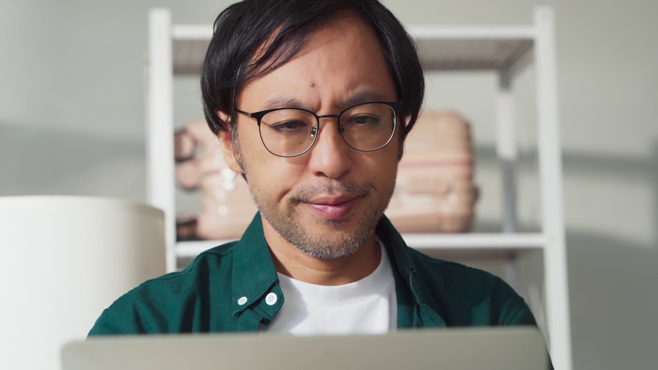 压力日本亚裔男性在家里用笔记本电脑工作，不开心，消极的工作项目麻烦，悲伤，焦虑，担心严重的在家工作