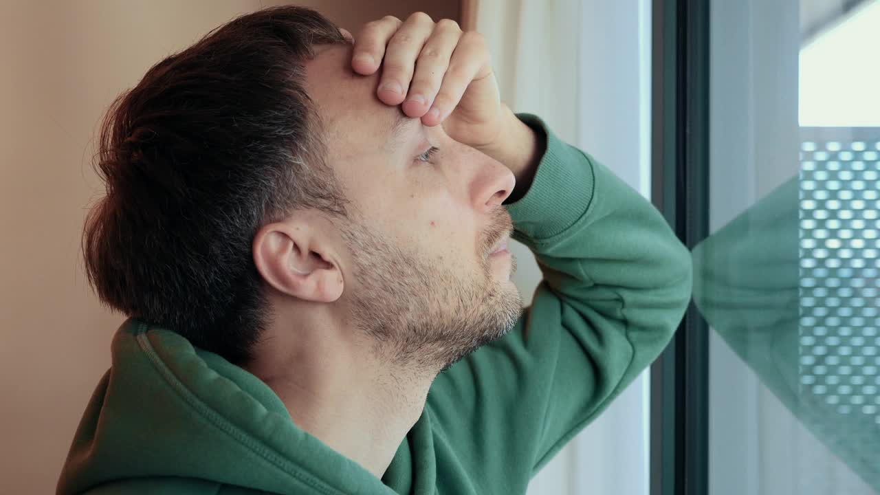 孤独的中年男人担心问题，收到坏消息，看着窗户，用手揉额头，压力和担忧的概念