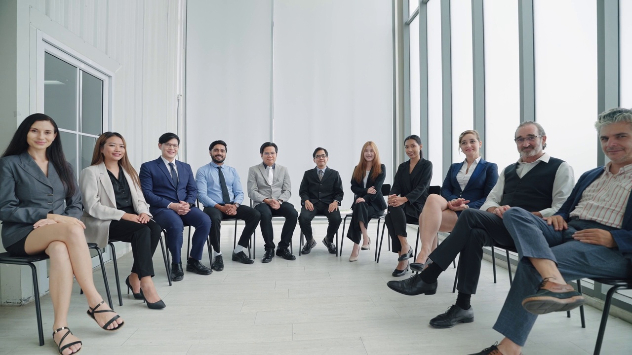 一群不同的公司同事一起坐在现代办公室里。成功的公司与商业团体的人微笑着看着镜头。商业专业人士的混合年龄组