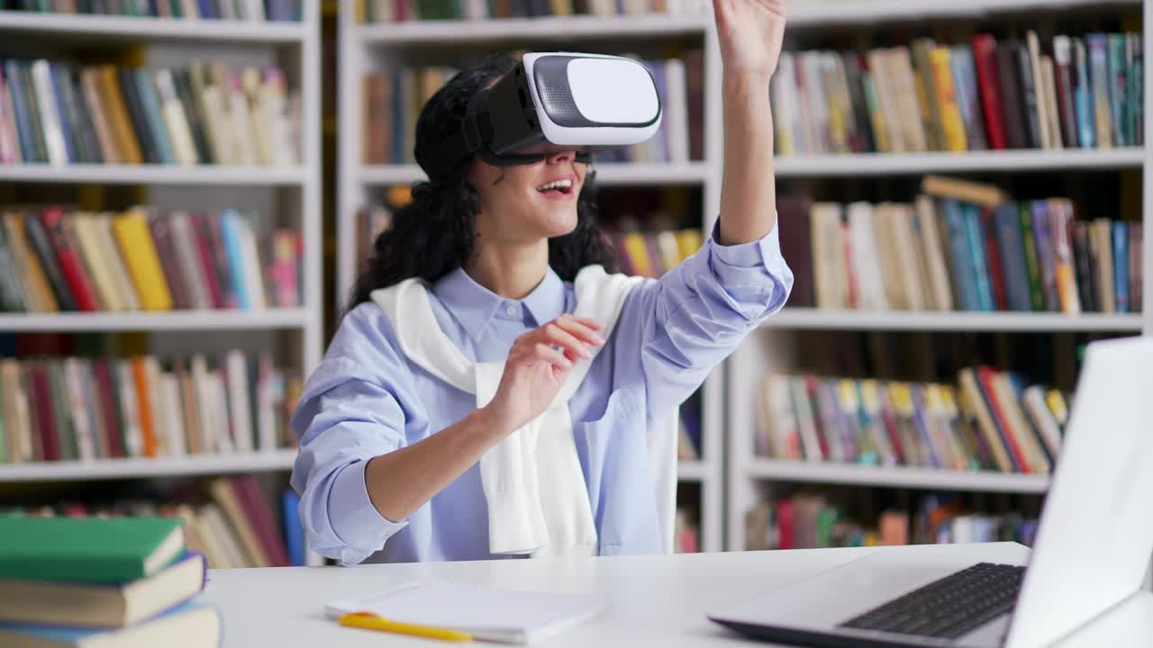 成功的女学生坐在校园图书馆的虚拟现实模拟器中使用VR眼镜进行创作