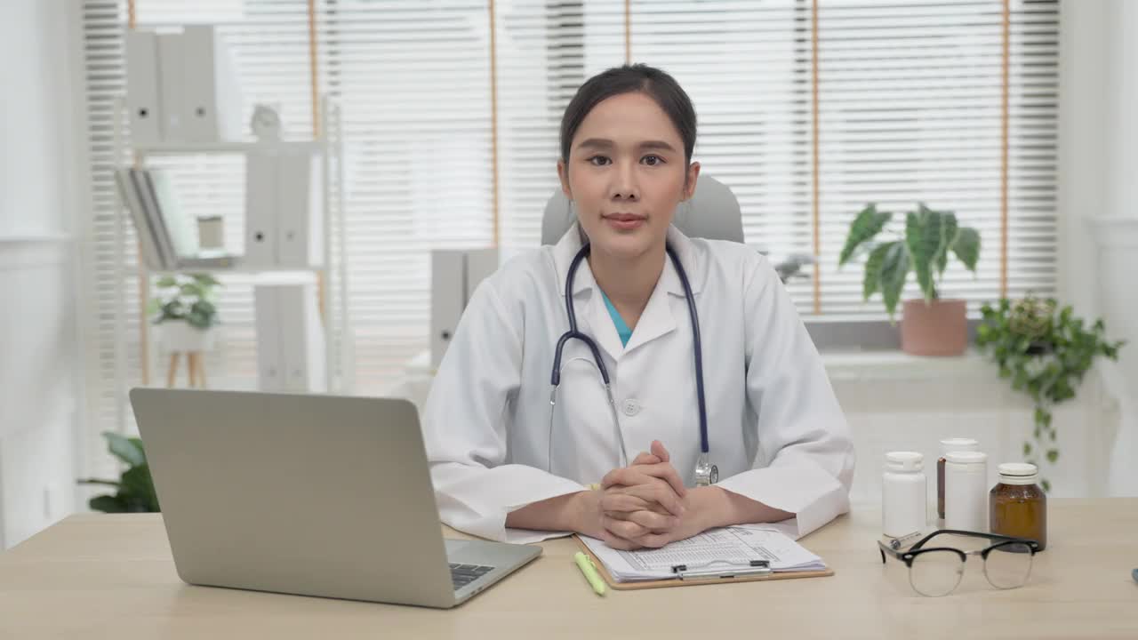年轻的亚洲女子穿着医生制服，在诊所自信地微笑，看着镜头微笑。