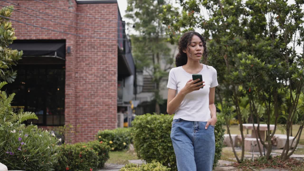 一个非裔美国少女走在花园里讲电话。现代通信技术，智能手机，高速互联网。假期里散散步