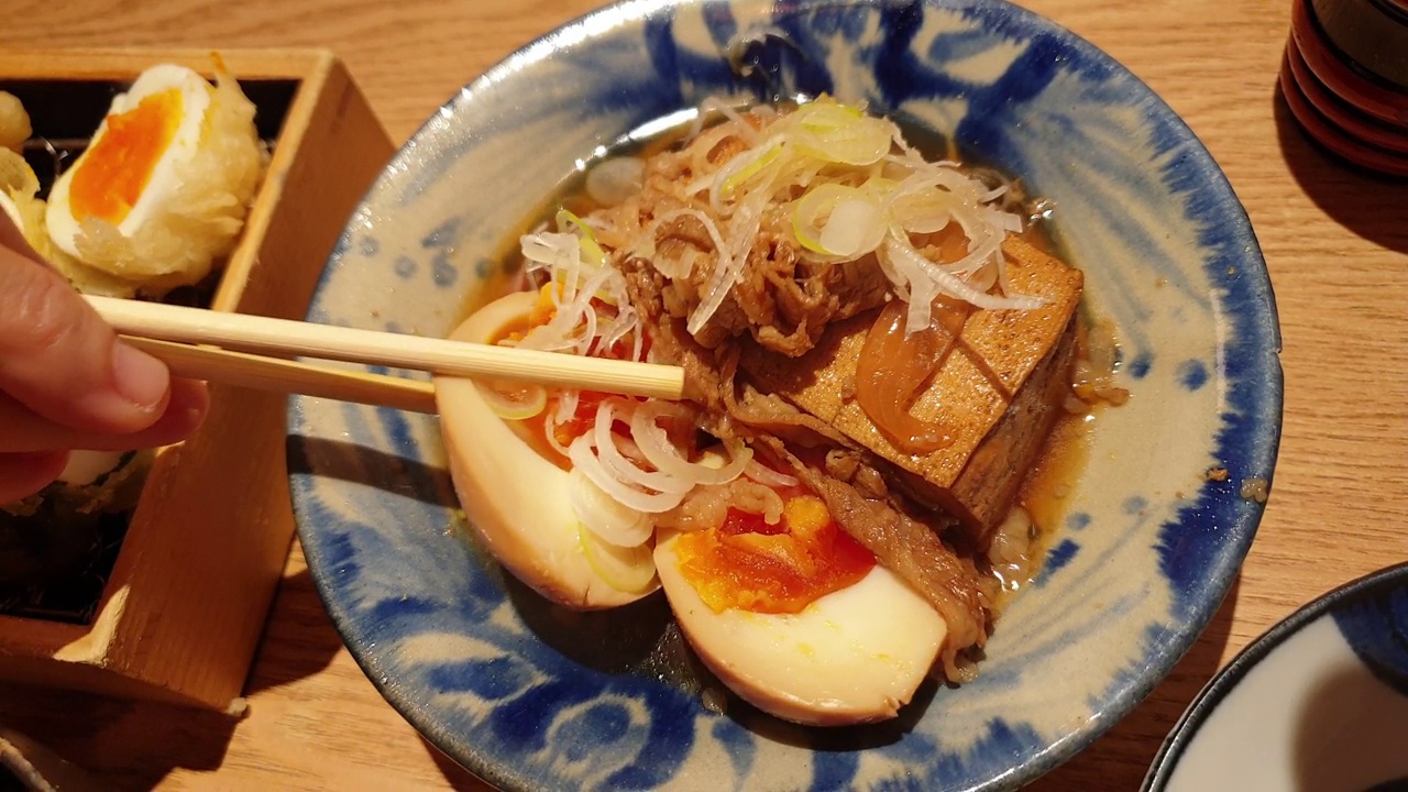 用手筷子吃小配菜的日本居酒屋料理豆腐炖牛肉和鸡蛋菜4k