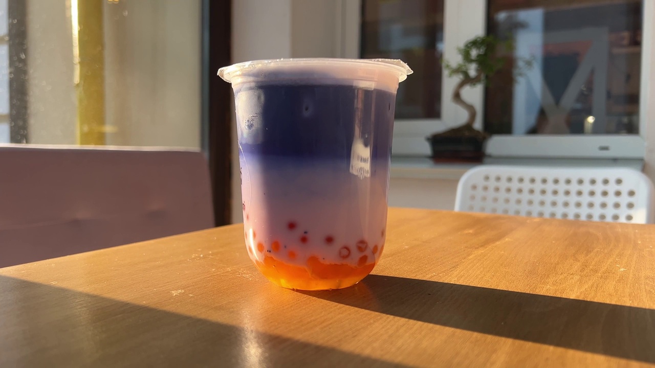 在阳光明媚的街道上，在木桌上喝着丁香蓝色的橙球奶茶