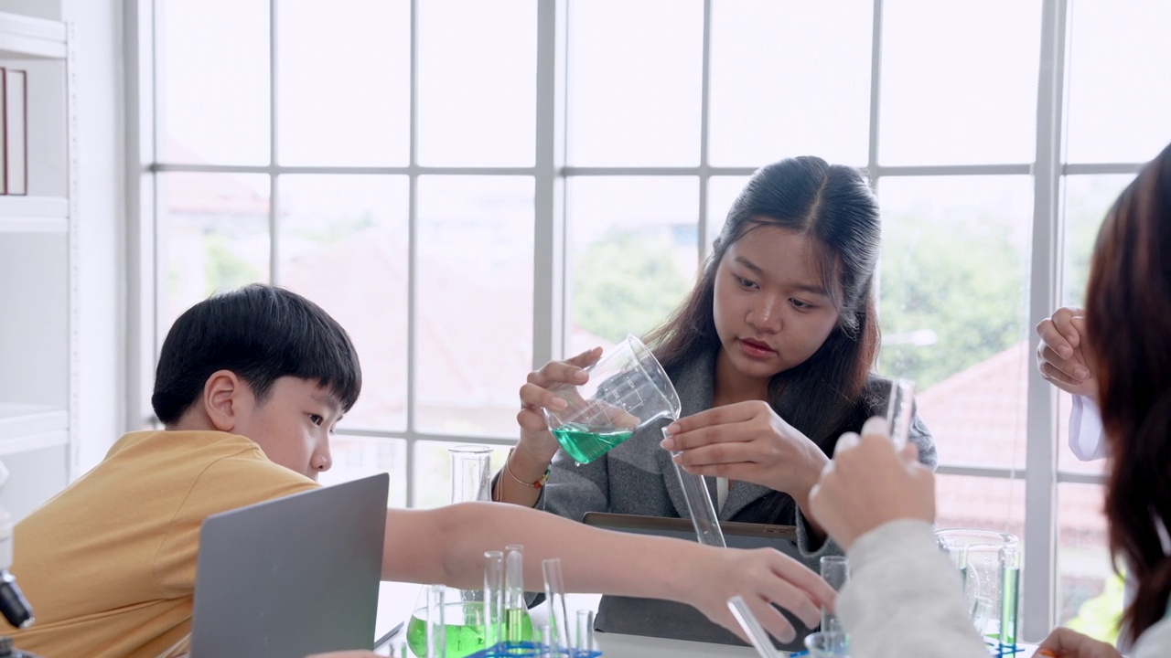 可爱的亚洲女学生在教室里和朋友们一起在科学试管里试验调色。在学校实验室学习实验，有老师在旁边指导