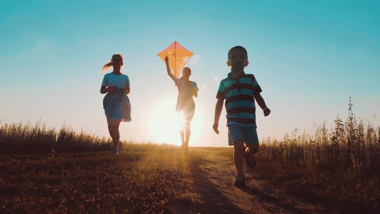 詳情圖-快樂的年輕媽媽帶著孩子們一起在公園里放風(fēng)箏。男孩手里拿著風(fēng)箏在跑。夕陽下公園里快樂的人們奔跑的剪影。幸福父母童年夢(mèng)想概念。