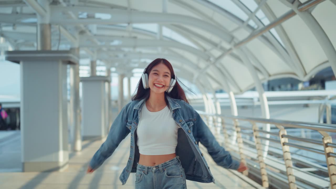 詳情圖-快樂的年輕亞洲女子戴著耳機(jī)在的街道上欣賞音樂，微笑的女性獨(dú)自聽音樂跳舞。