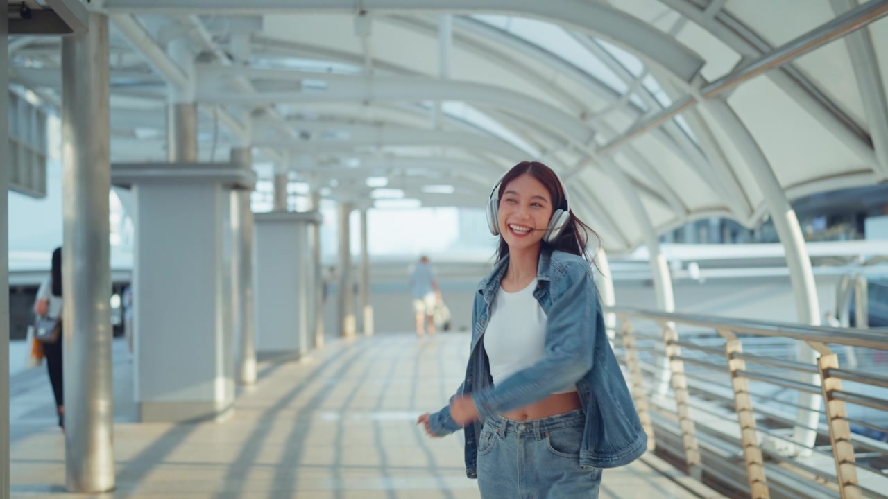 詳情圖-快樂的年輕亞洲女子戴著耳機(jī)在的街道上欣賞音樂，微笑的女性獨(dú)自聽音樂跳舞。