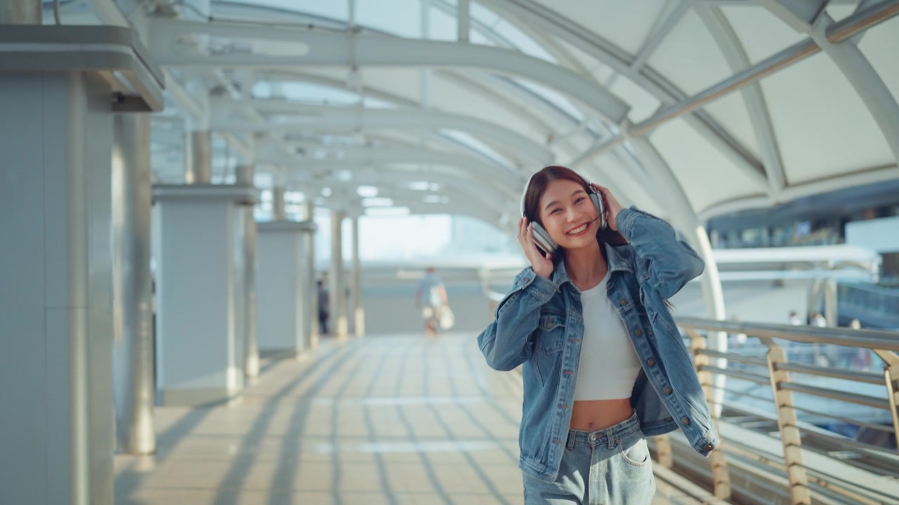 詳情圖-快樂的年輕亞洲女子戴著耳機(jī)在的街道上欣賞音樂，微笑的女性獨(dú)自聽音樂跳舞。