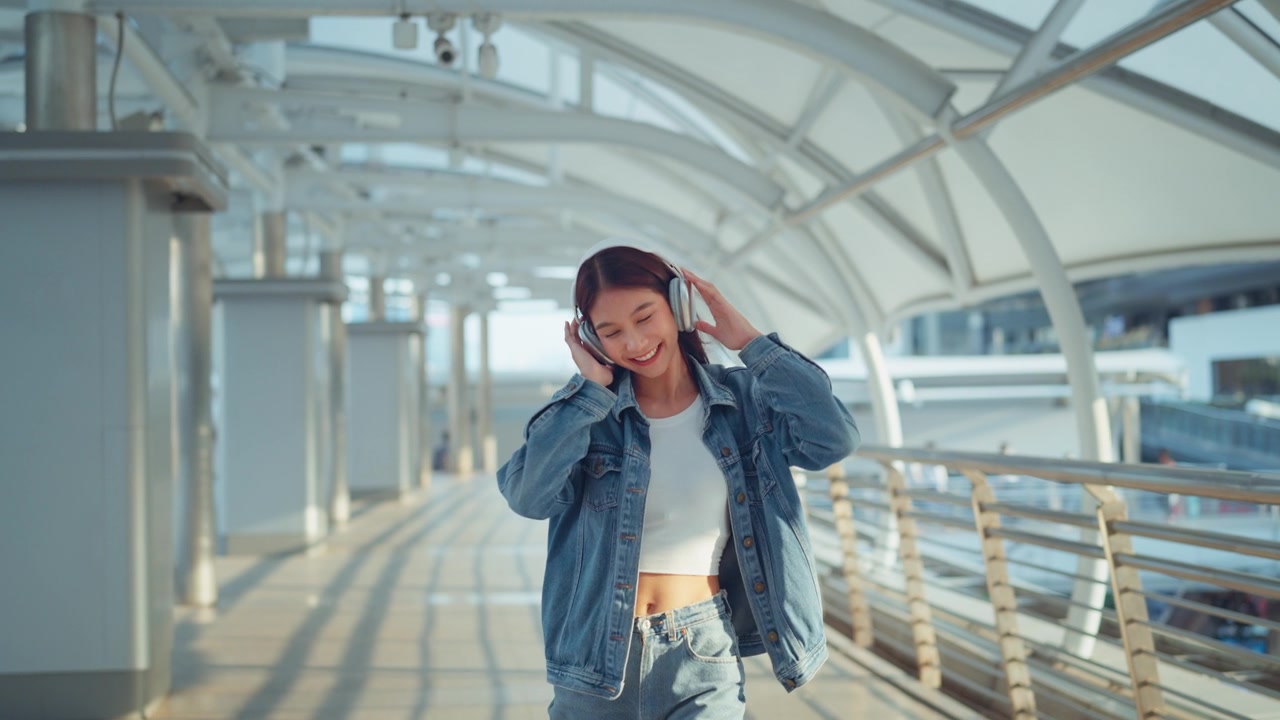 詳情圖-快樂的年輕亞洲女子戴著耳機(jī)在的街道上欣賞音樂，微笑的女性獨(dú)自聽音樂跳舞。
