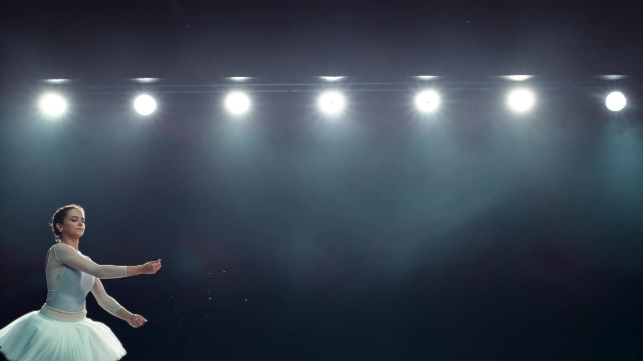 灯光大舞台上美丽的芭蕾舞表演。年轻的女芭蕾舞演员在白色的裙子做一个完美的劈叉跳跃和释放粉末。超级慢动作速度斜坡效果
