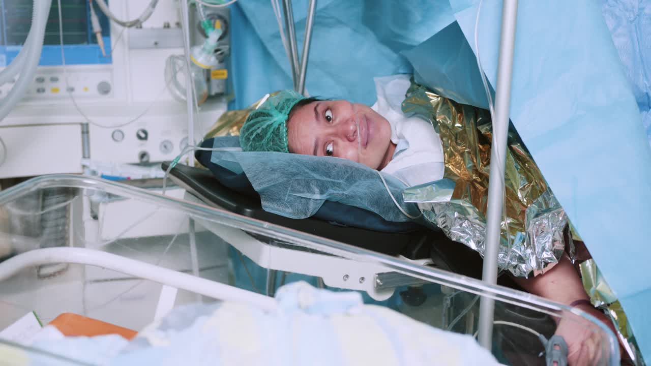 医院里母亲抱着刚出生的婴儿。刚分娩的母亲把刚出生的婴儿抱在胸前。第一眼看到手术室里的妈妈和她的新生儿。现代医院手术室。