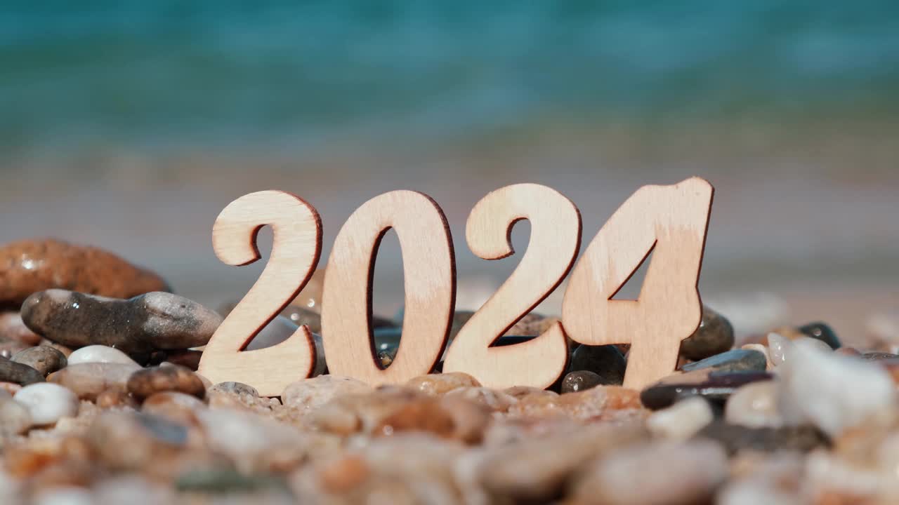 海边沙滩上的木制新年数字2024特写，背景是海浪和冲浪。